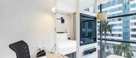 Una habitación de hotel moderna con escritorio, silla, cama y ventanas amplias con vistas a la ciudad.