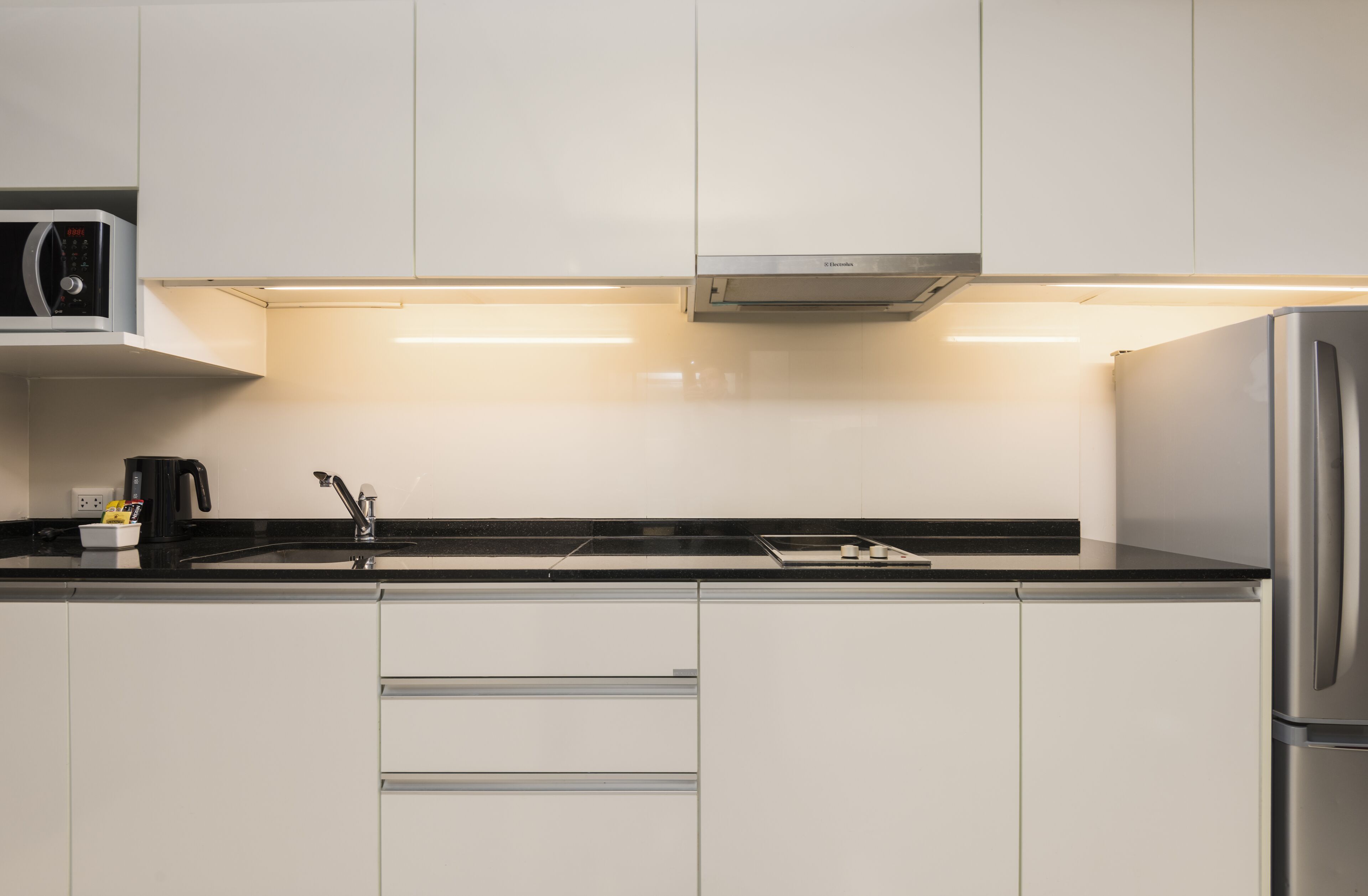 Una cocina moderna con armarios blancos, un refrigerador de acero inoxidable, un microondas y una cafetera.
