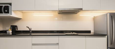 Una cocina moderna con armarios blancos, un refrigerador de acero inoxidable, un microondas y una cafetera.
