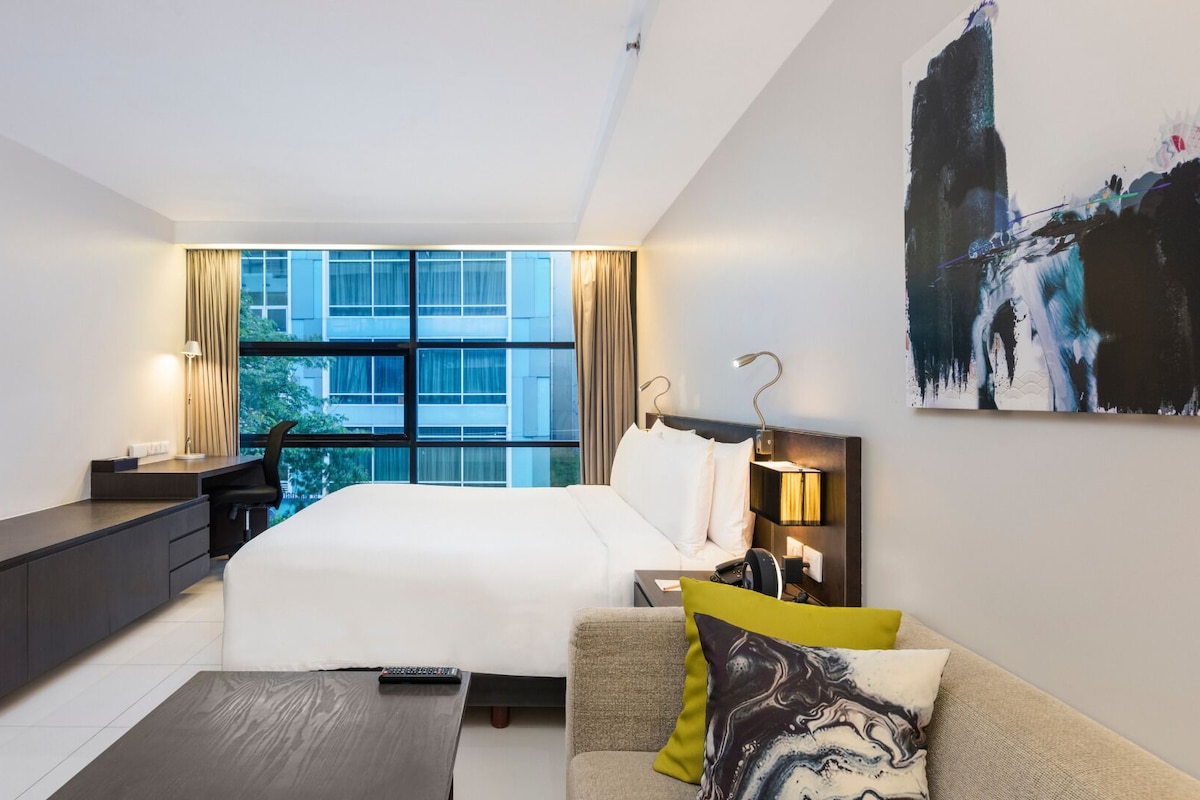 A modern hotel room with a large bed, a desk, a sofa, and a TV.