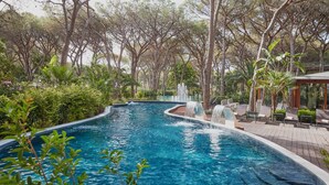A swimming pool with a waterfall feature, surrounded by lush greenery and trees. - Forte Village Resort – Hotel Pineta (Pula)