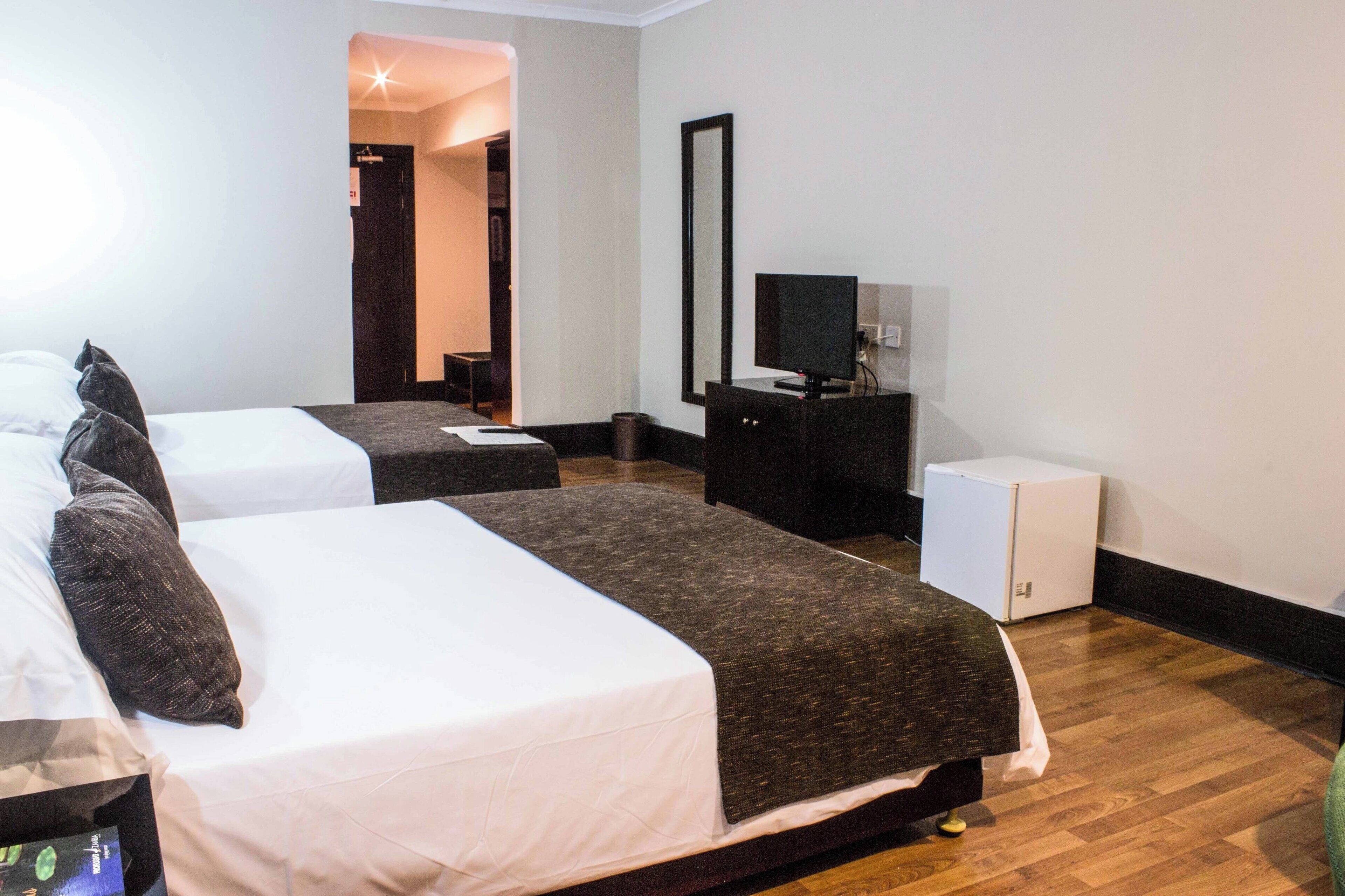 A hotel room with two beds, a television, a small cabinet, and a mirror.