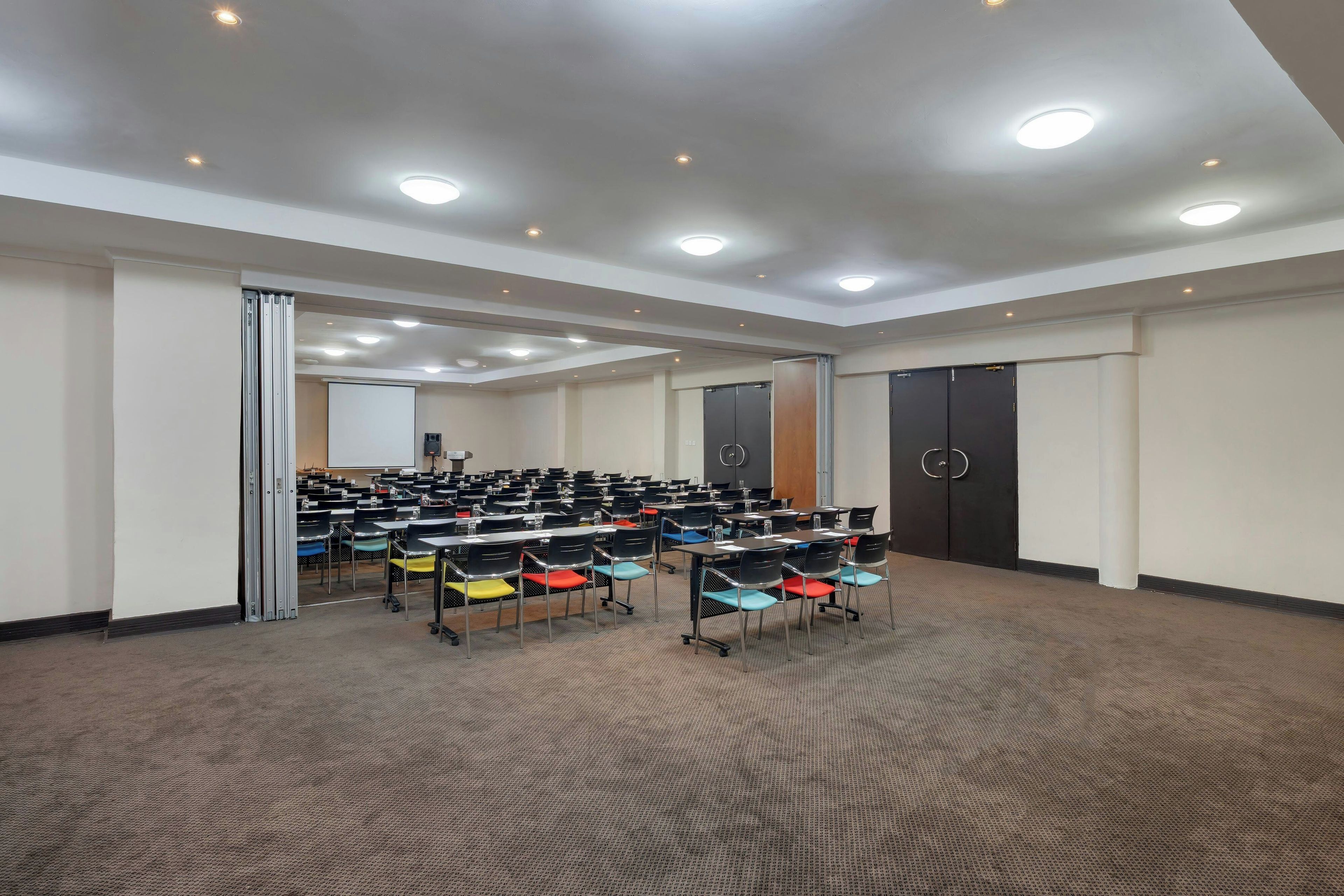 A conference room with rows of tables and chairs, a whiteboard, and a projector.