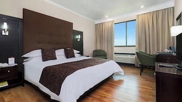 Quarto de hotel com uma cama grande, uma escrivaninha, uma cadeira e vista para o exterior.