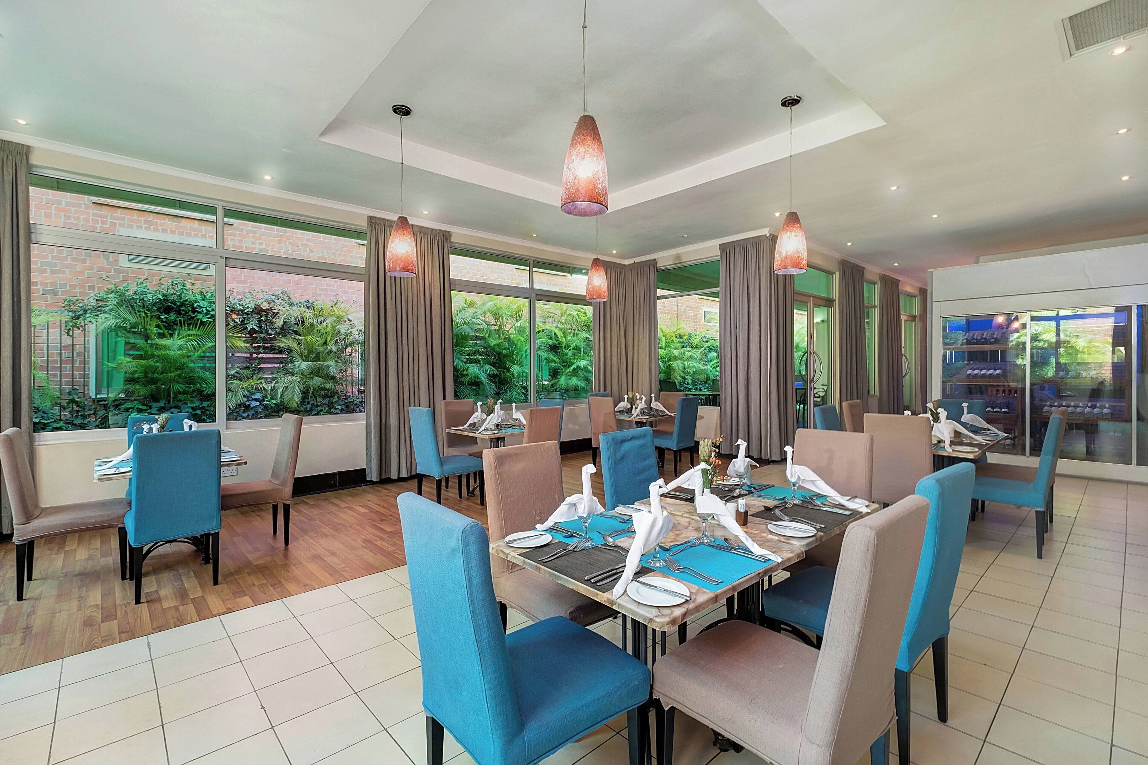 A restaurant with tables set for dining, large windows, and hanging pendant lights.