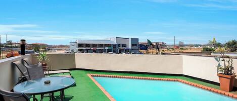 A rooftop pool with a glass table and chairs, surrounded by a green artificial turf area.