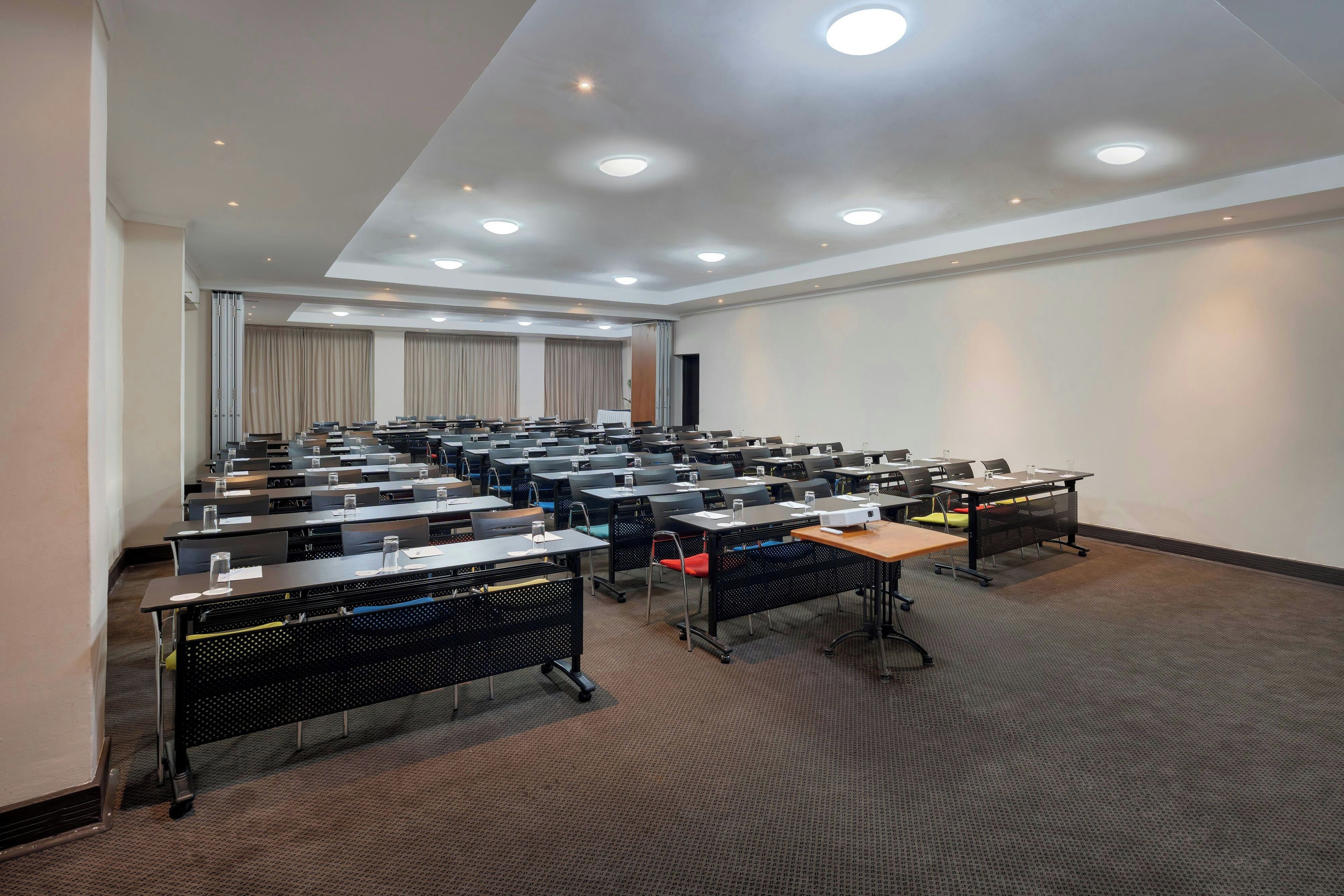 Un salón de conferencias con varias mesas y sillas, equipado con proyectores y botellas de agua.