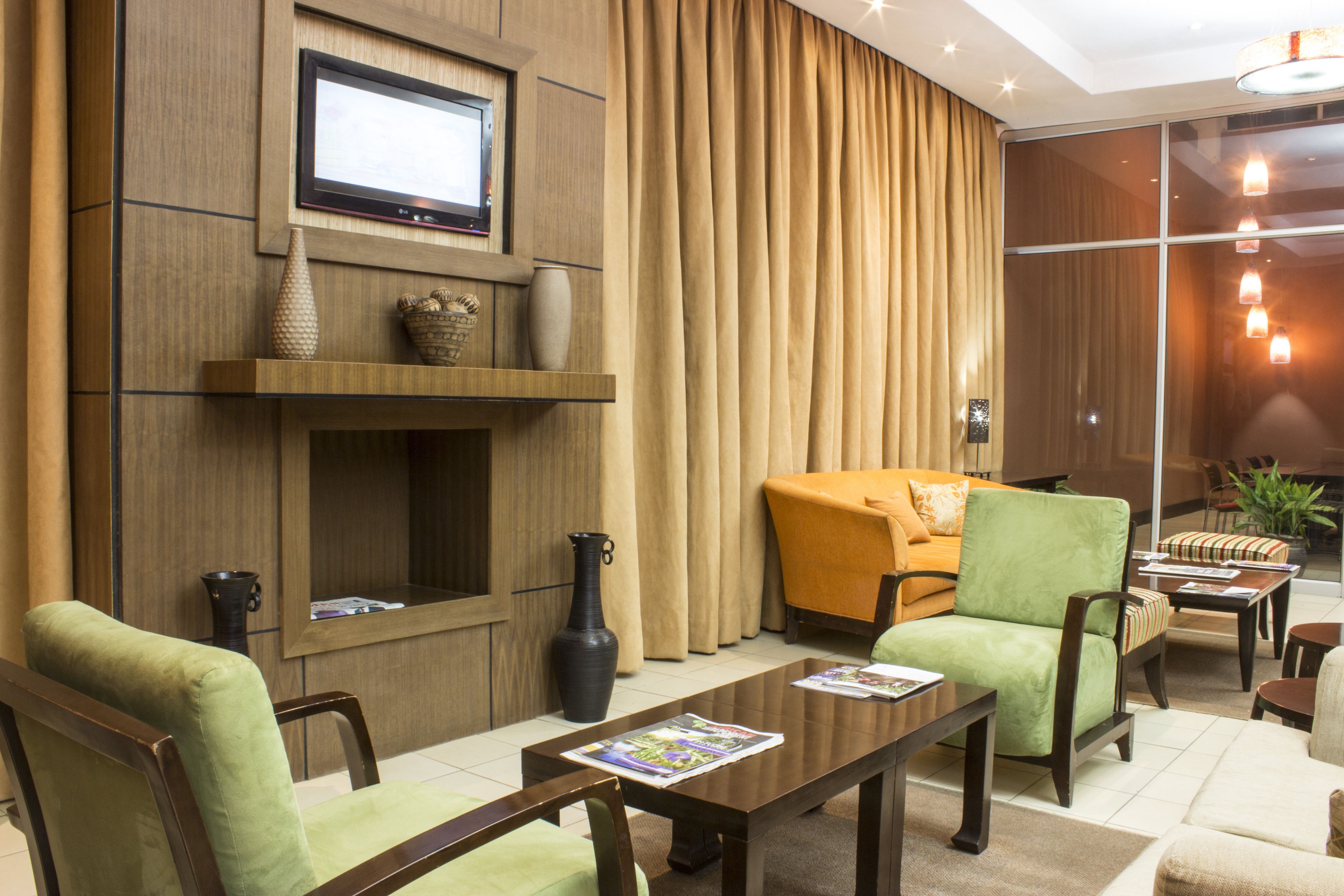 A modern living room with a television, a fireplace, comfortable seating, and a large window with curtains.