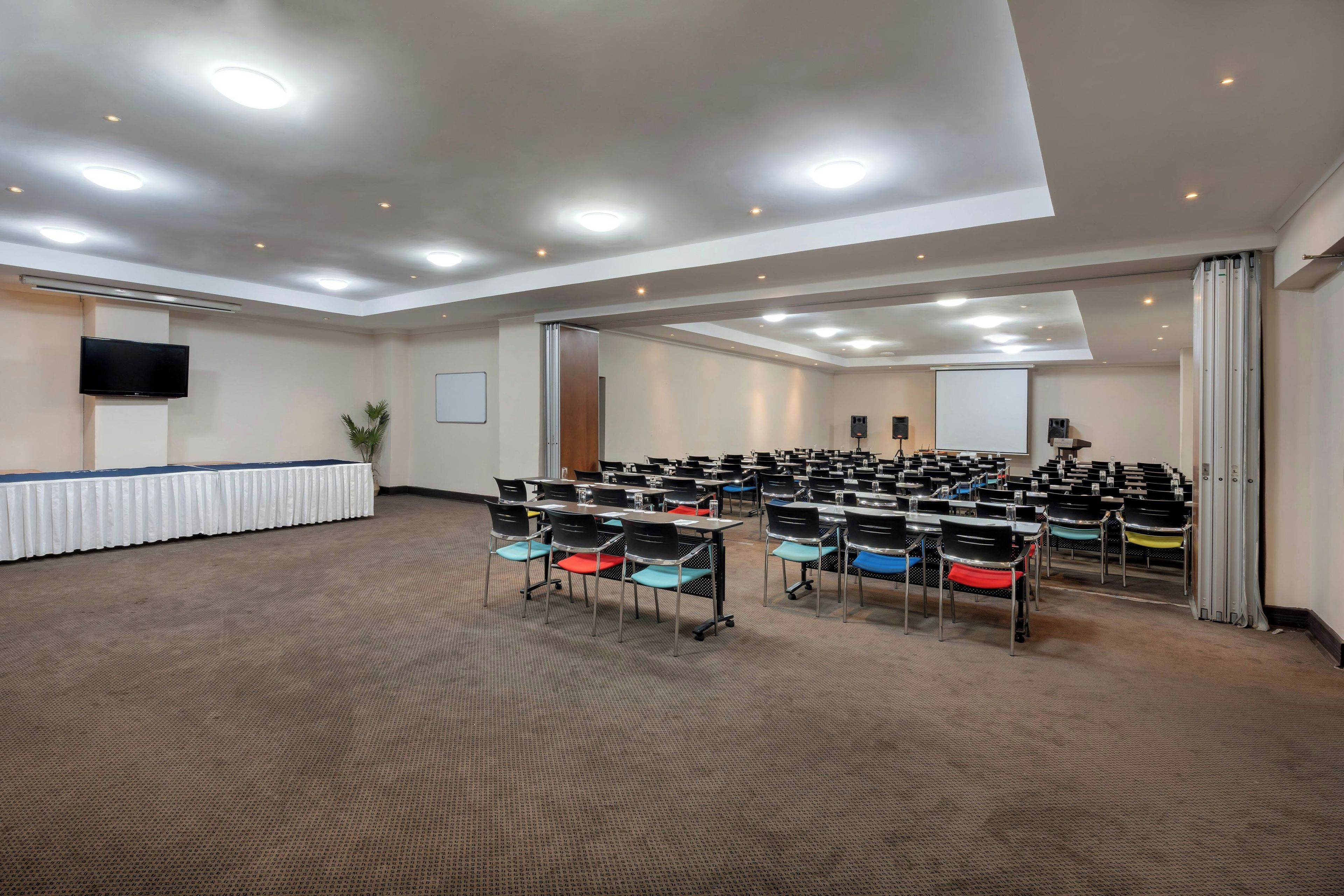 Un salón de conferencias con filas de sillas, una pizarra y un televisor de pantalla plana en la pared.