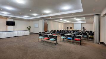 Un salón de conferencias con filas de sillas, una pizarra y un televisor de pantalla plana en la pared.