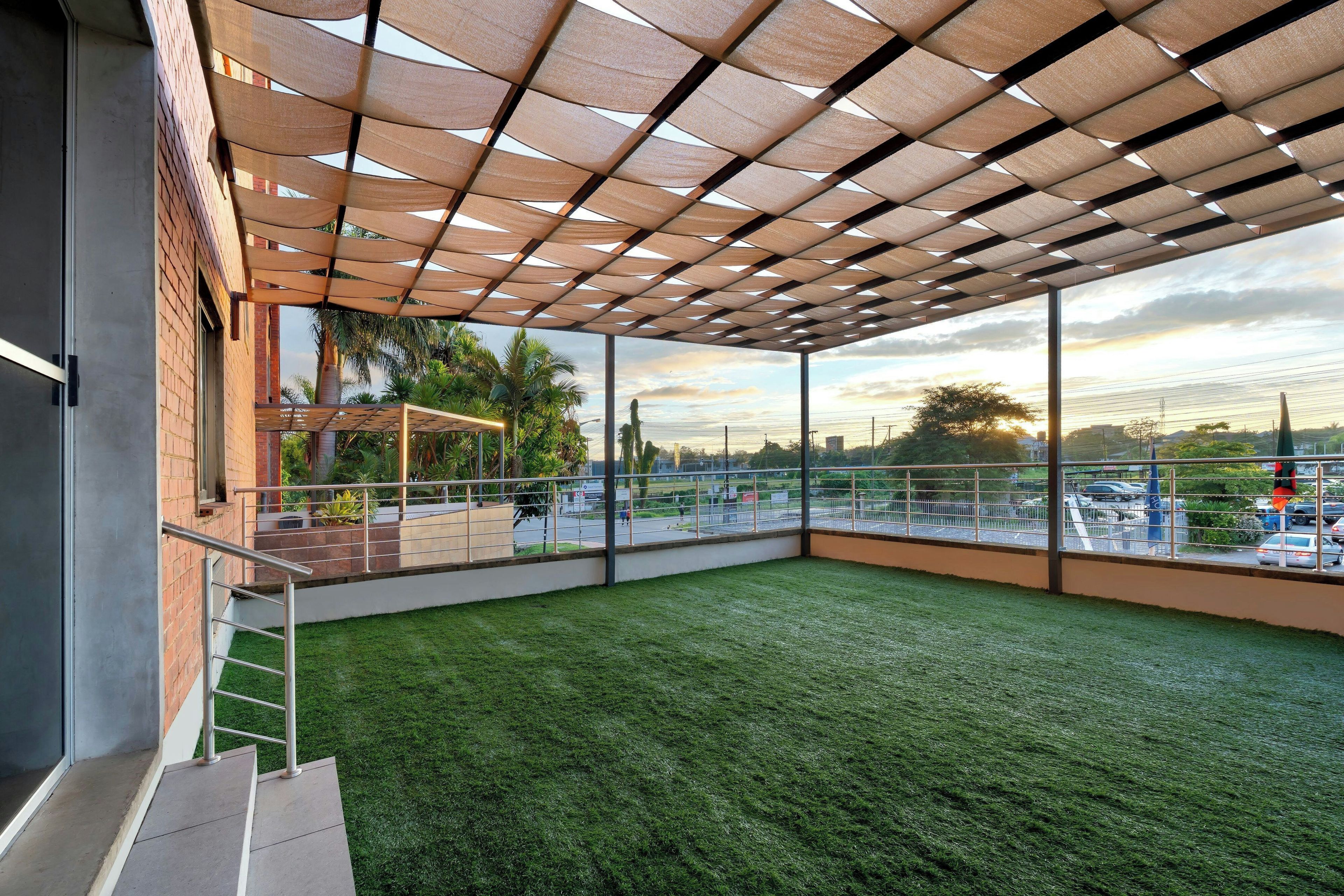 A covered outdoor area with a view of a cityscape, a grassy lawn, and a metal railing.