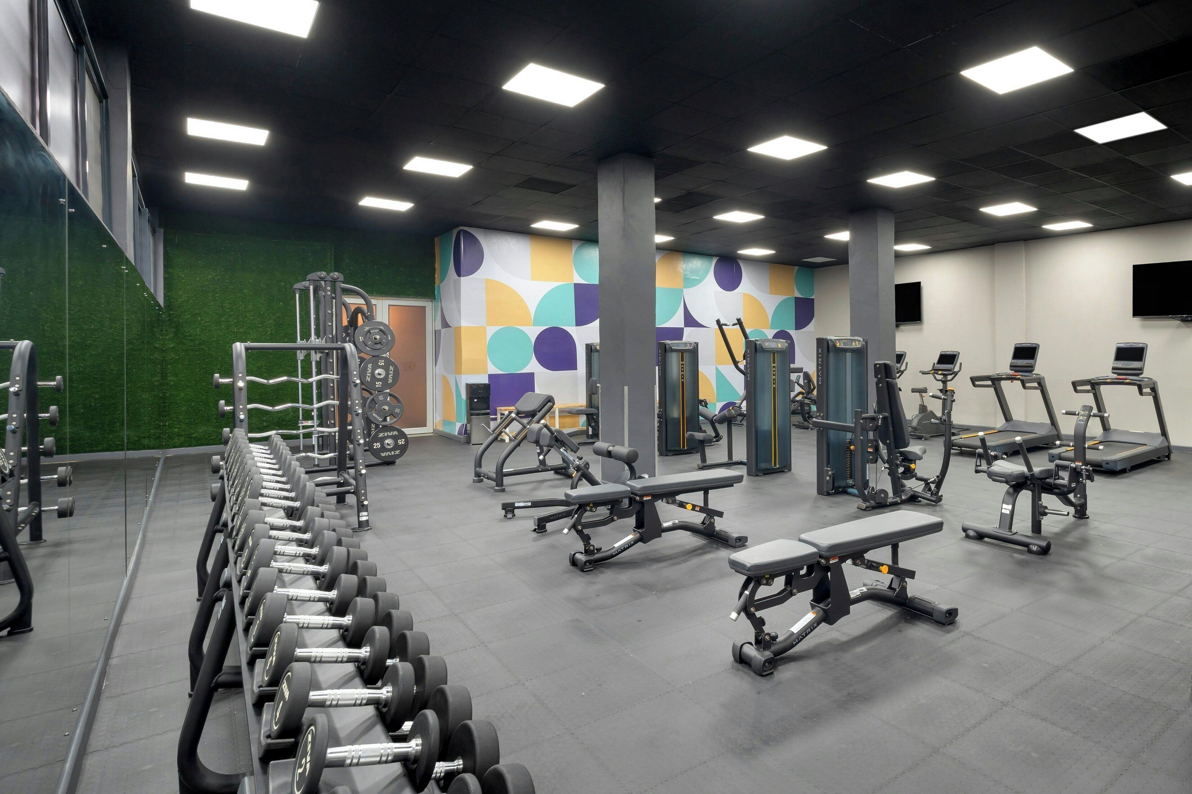 Una palestra con diverse attrezzature per esercizi, tra cui manubri, panche e tapis roulant.