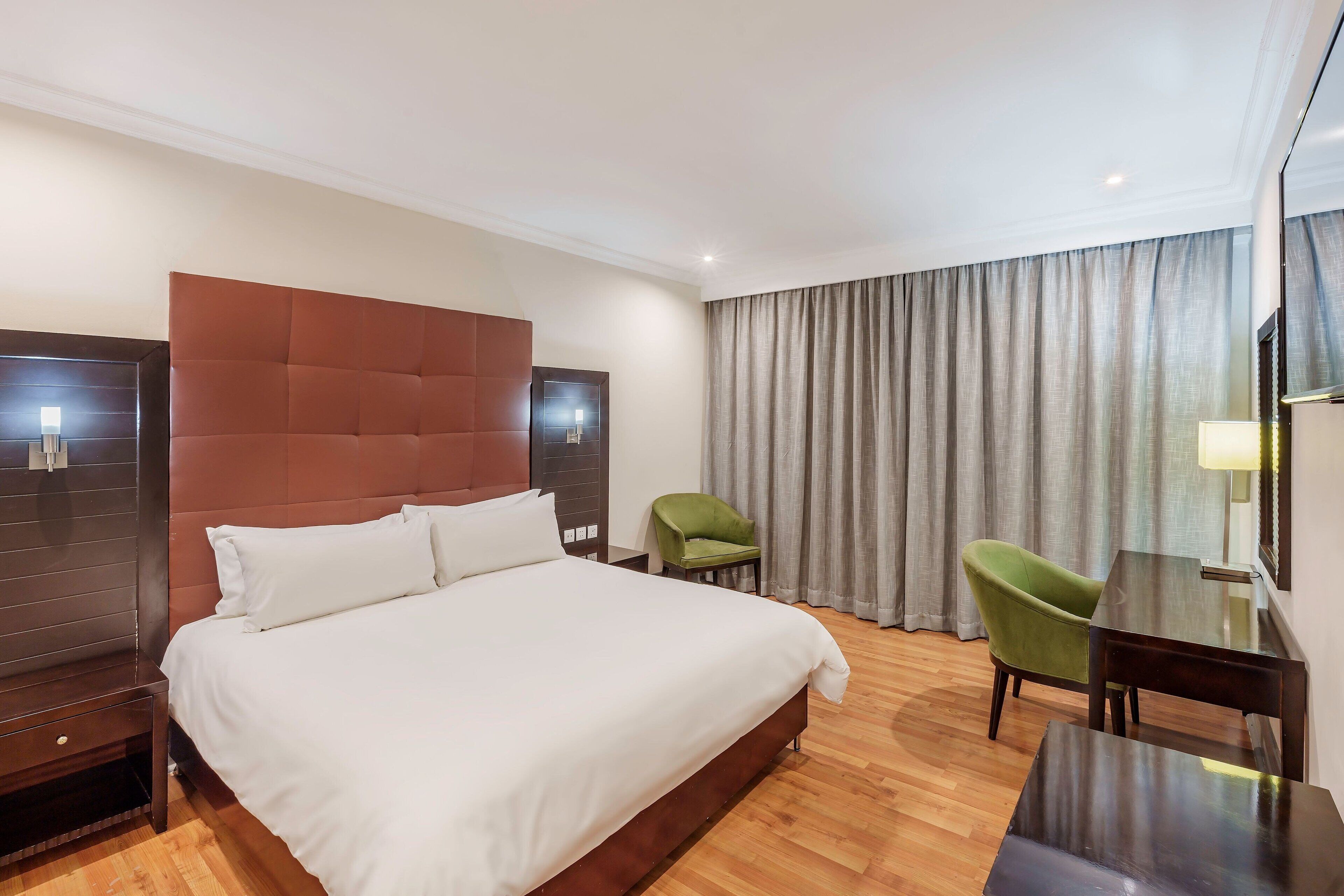 A hotel room with a large bed, a desk, two chairs, and a curtain.