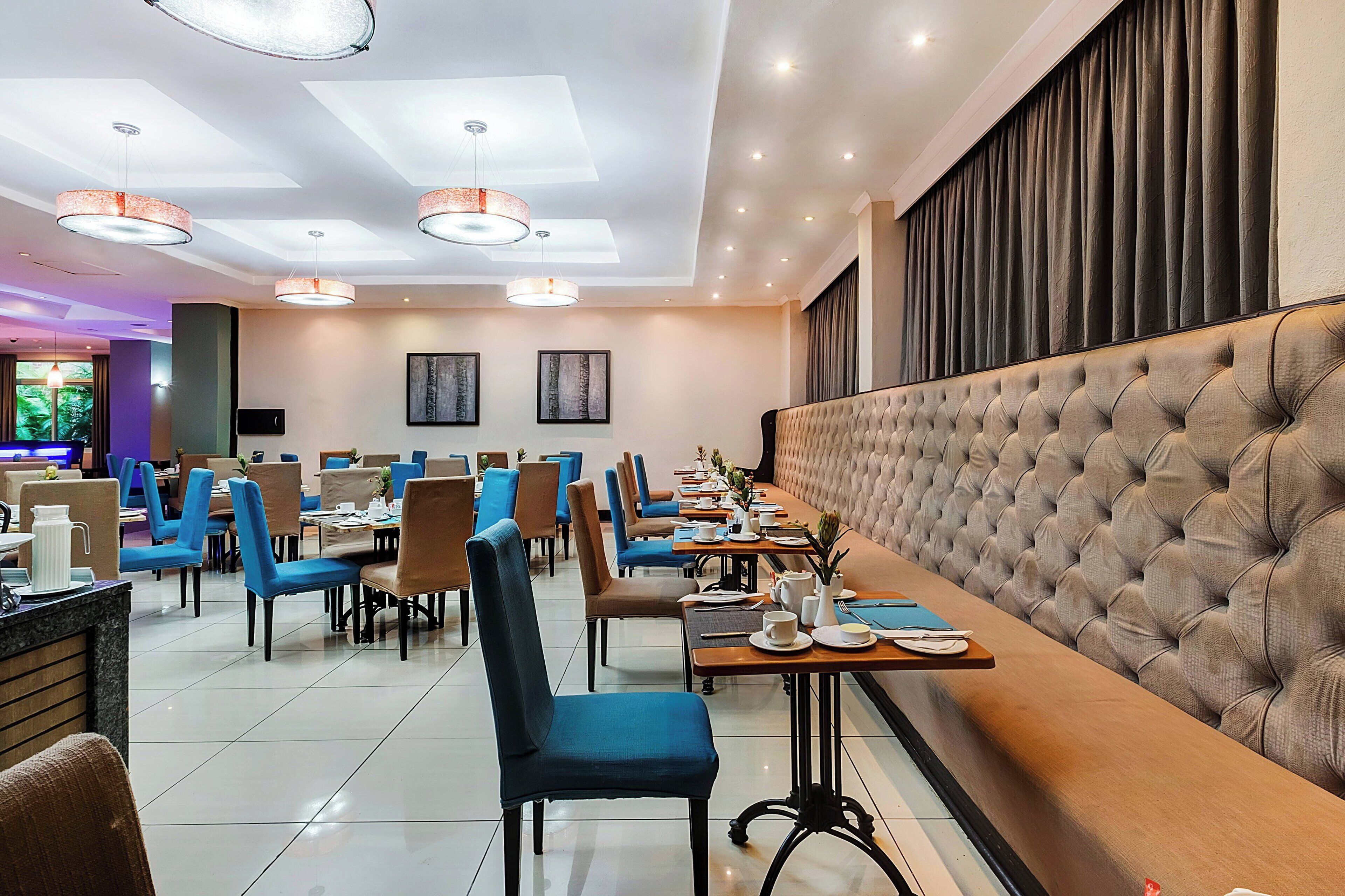 A modern restaurant with blue chairs, wooden tables, and a tufted headboard.