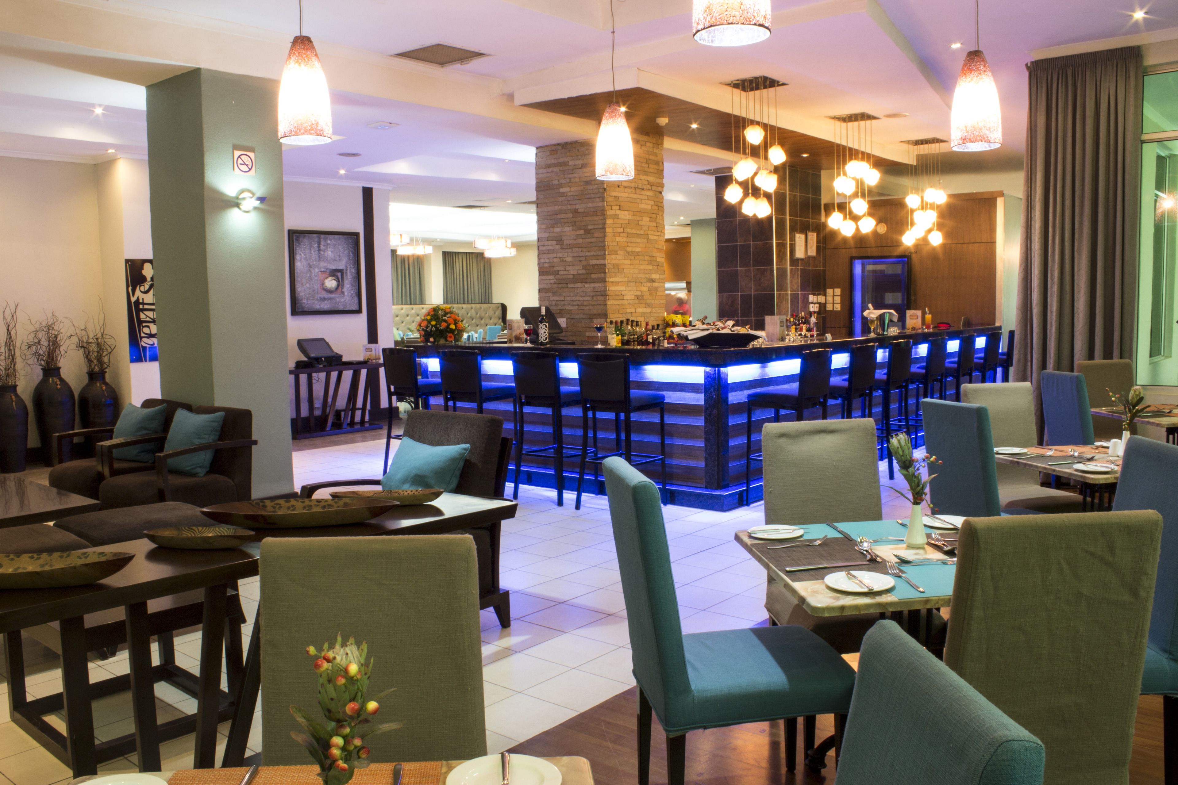 A modern hotel lobby with a bar area, seating arrangements, and a staircase leading to the upper floors.
