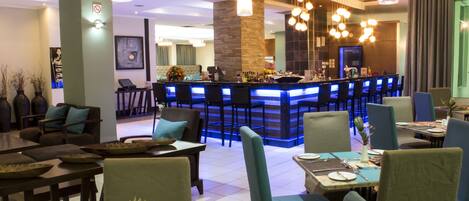 A modern hotel lobby with a bar area, seating arrangements, and a staircase leading to the upper floors.