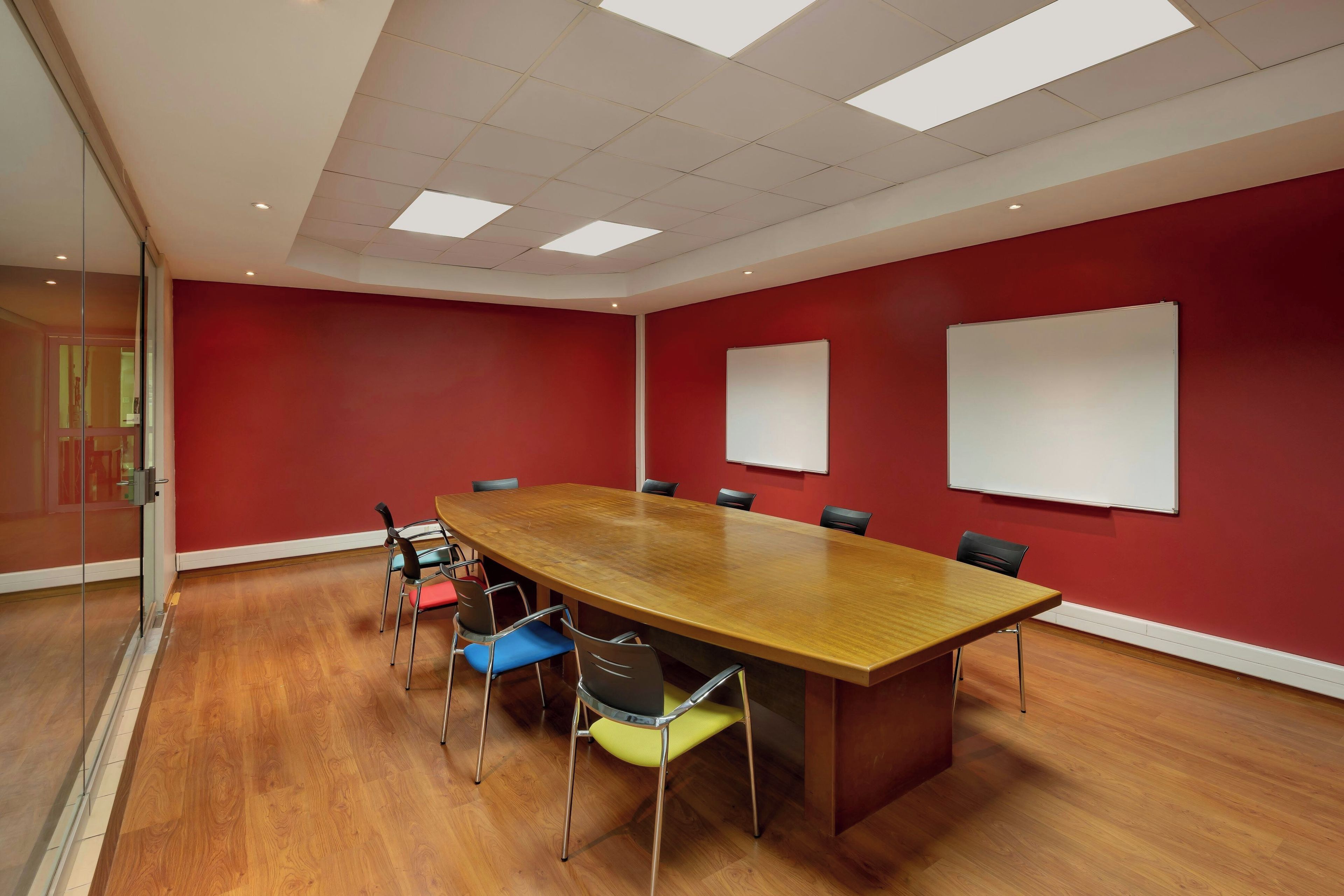 Una sala de conferencias con una amplia mesa de madera, paredes rojas y dos pizarras blancas.
