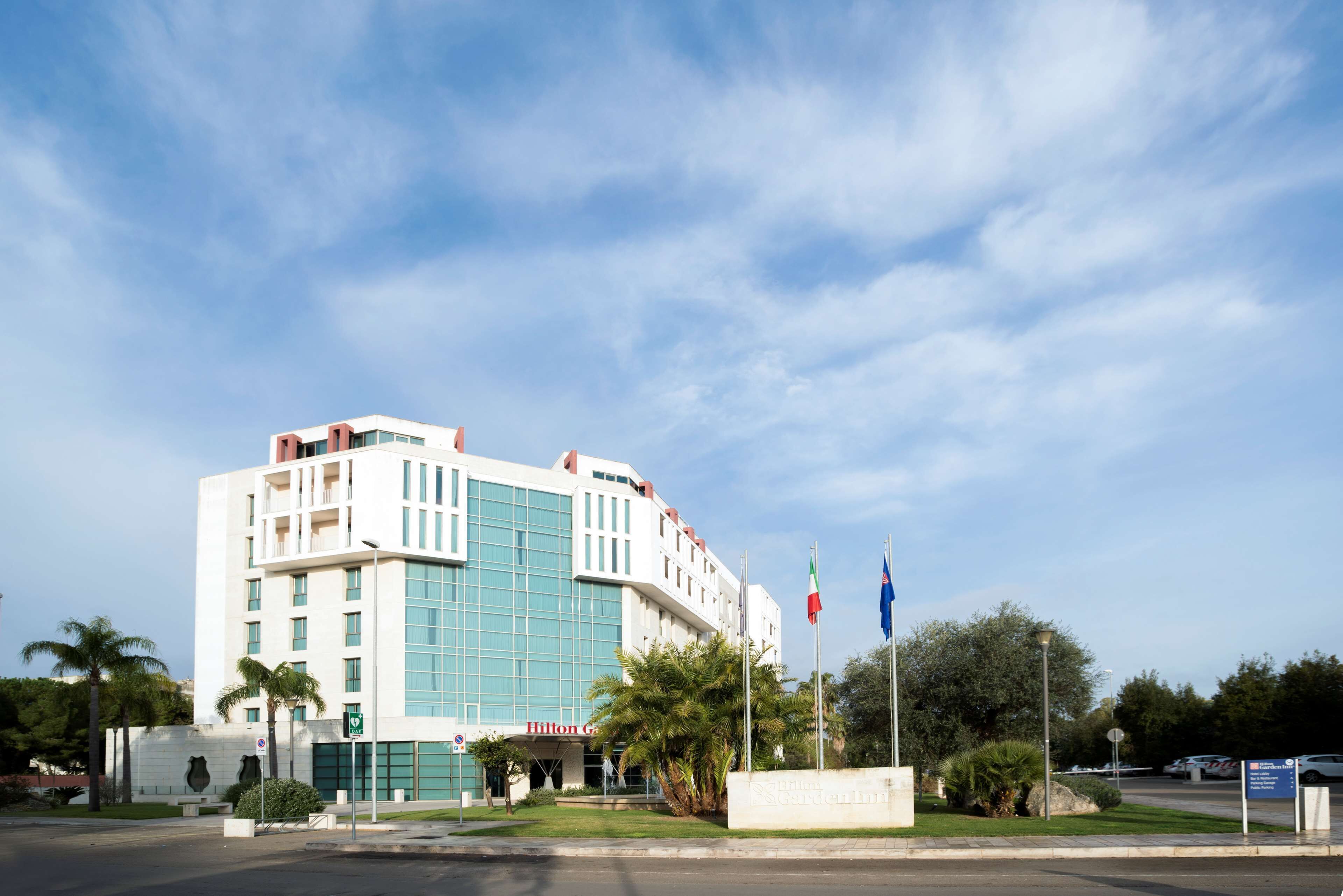 A modern hotel with a prominent glass facade, a well-maintained lawn, and a clear sky.