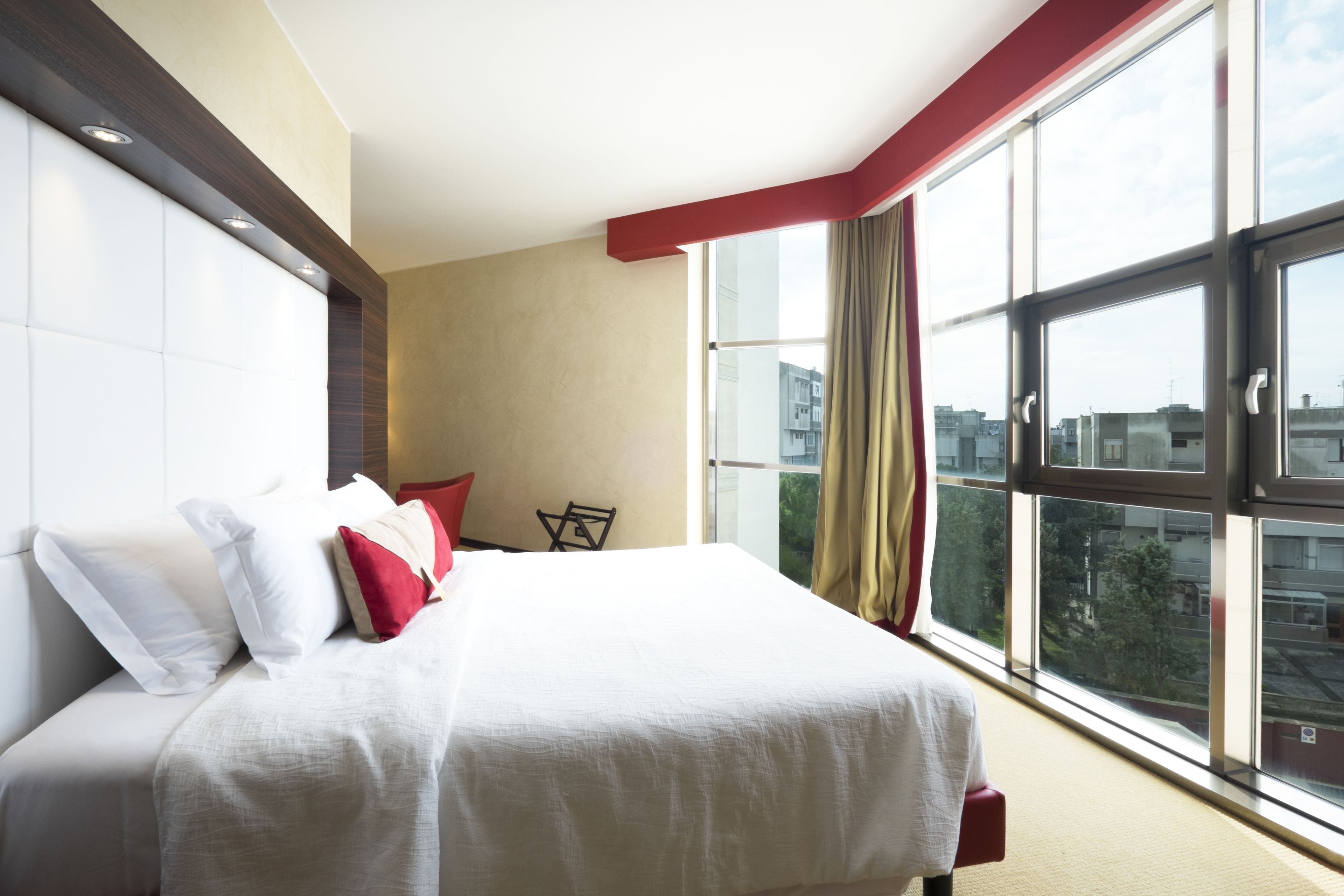 Une chambre d’hôtel avec un grand lit, une petite table et une vue sur la ville grâce à de grandes fenêtres.