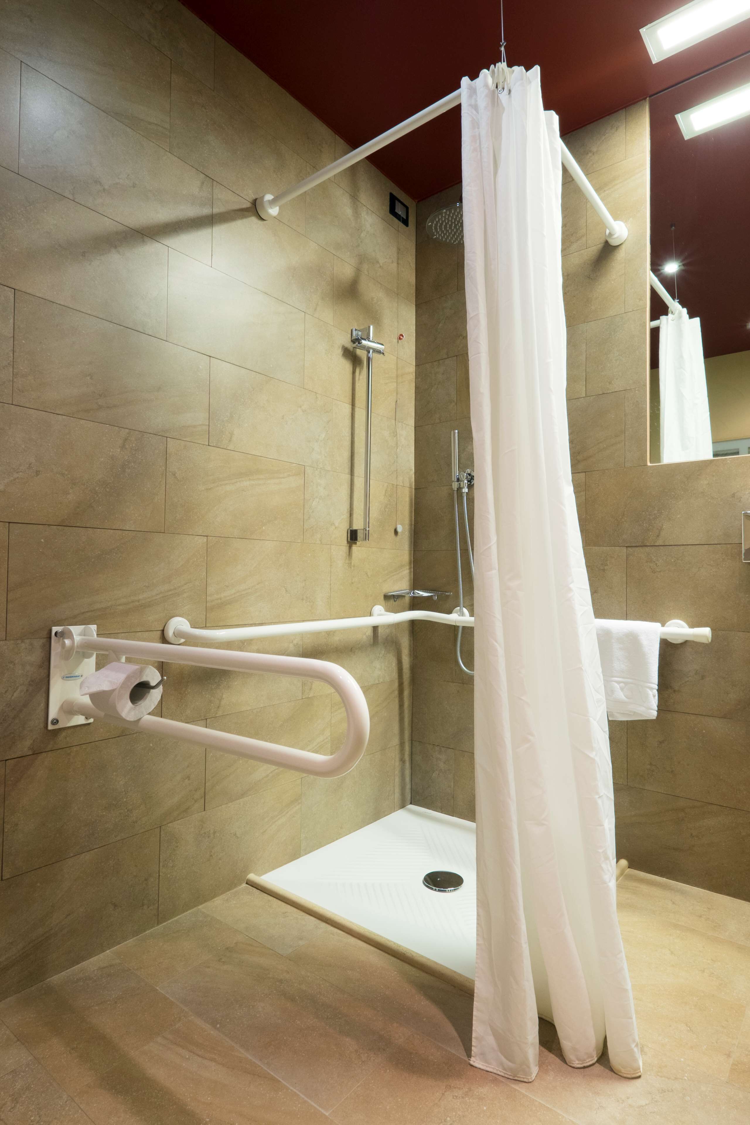 A shower area with a white shower curtain, grab bars, and a handheld showerhead.