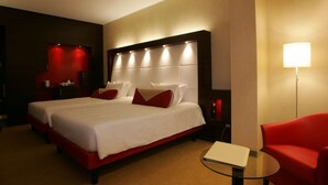 Habitación de hotel con una cama grande, un sillón rojo, una mesita y una lámpara de noche.