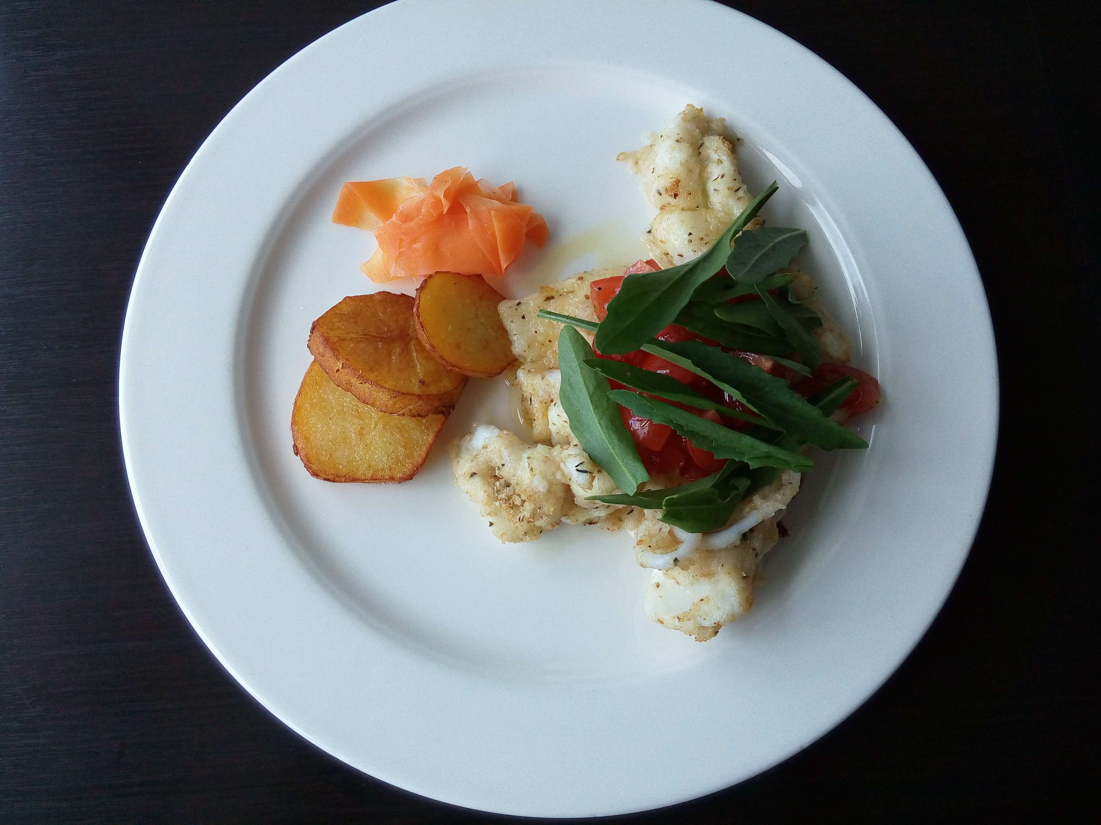 Un plato blanco con comida que incluye un pescado blanco, rodajas de patata naranja y verduras verdes.