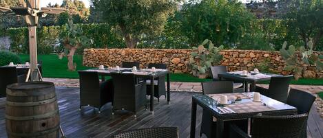 Un patio al aire libre con mesas y sillas, un muro de piedra y un barril de madera.