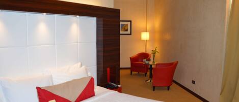 Ein Hotelzimmer mit einem großen Bett, einem Holz-Kopfteil, einem roten Sessel, einem kleinen Tisch mit einer Vase und einer Lampe.