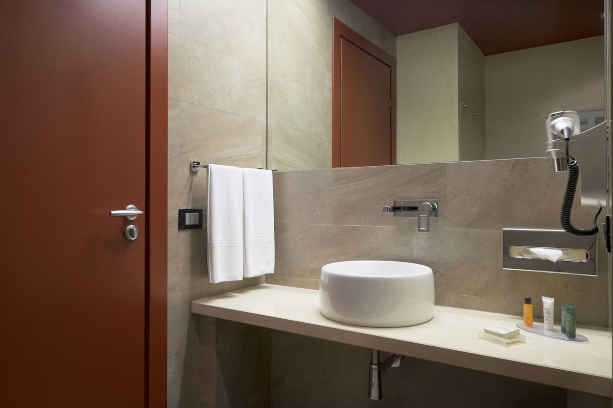 Un baño con un lavamanos blanco, una toalla colgada en un perchero, un espejo y una ducha con cabezal de ducha manual.