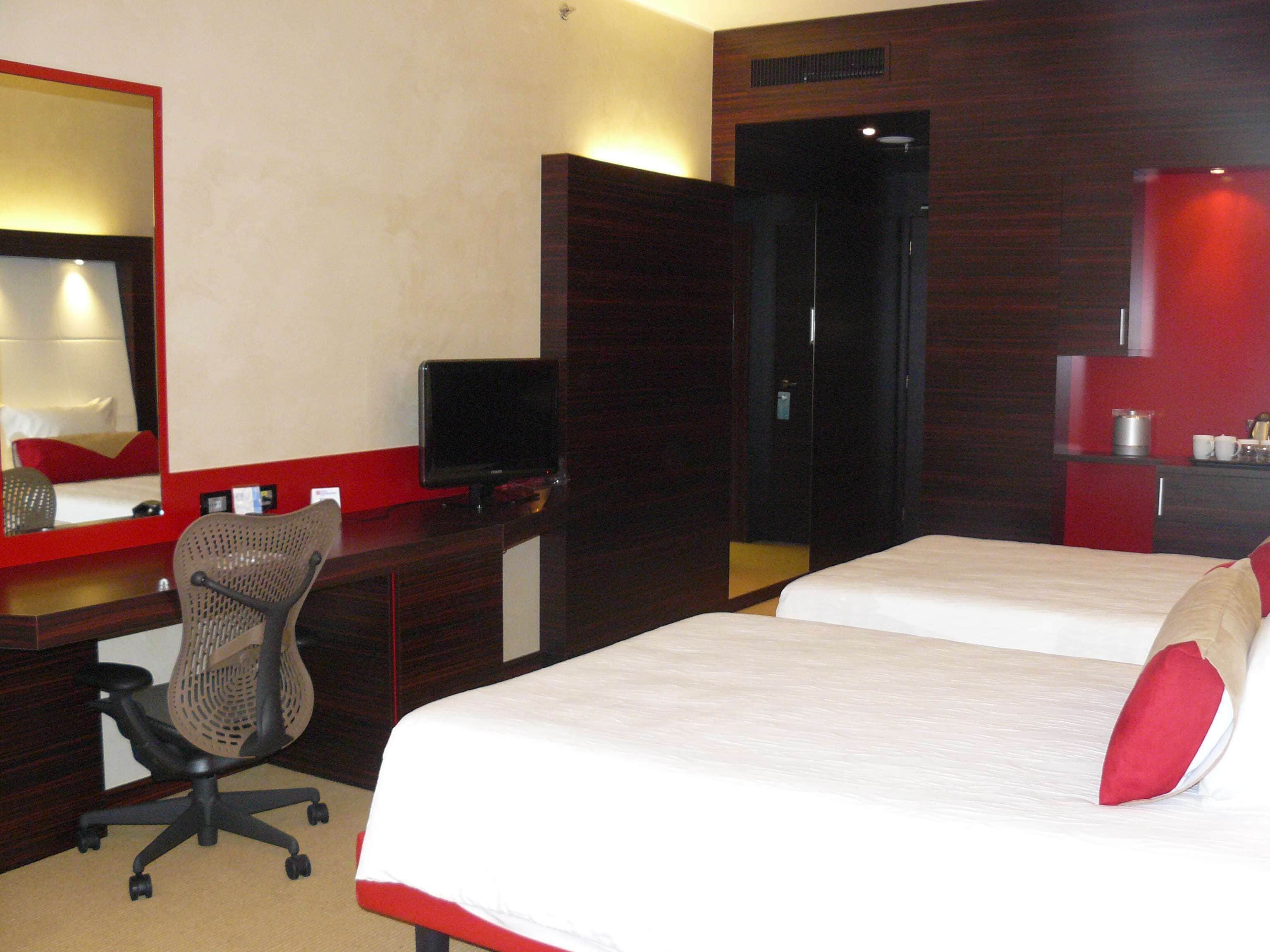 A hotel room with a bed, a desk with a computer, a chair, a TV, and a wardrobe.