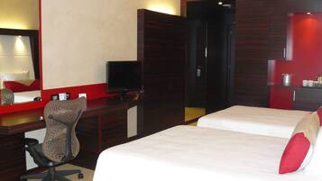 A hotel room with a bed, a desk with a computer, a chair, a TV, and a wardrobe.