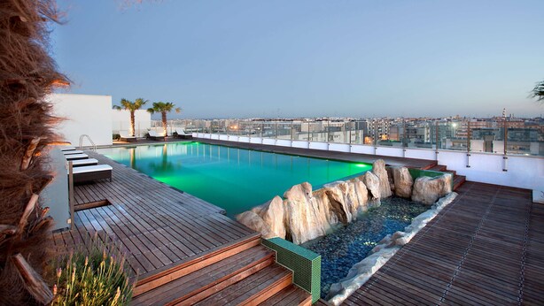 Una piscina en la azotea con terraza de madera, un elemento decorativo de roca y vistas a la ciudad.