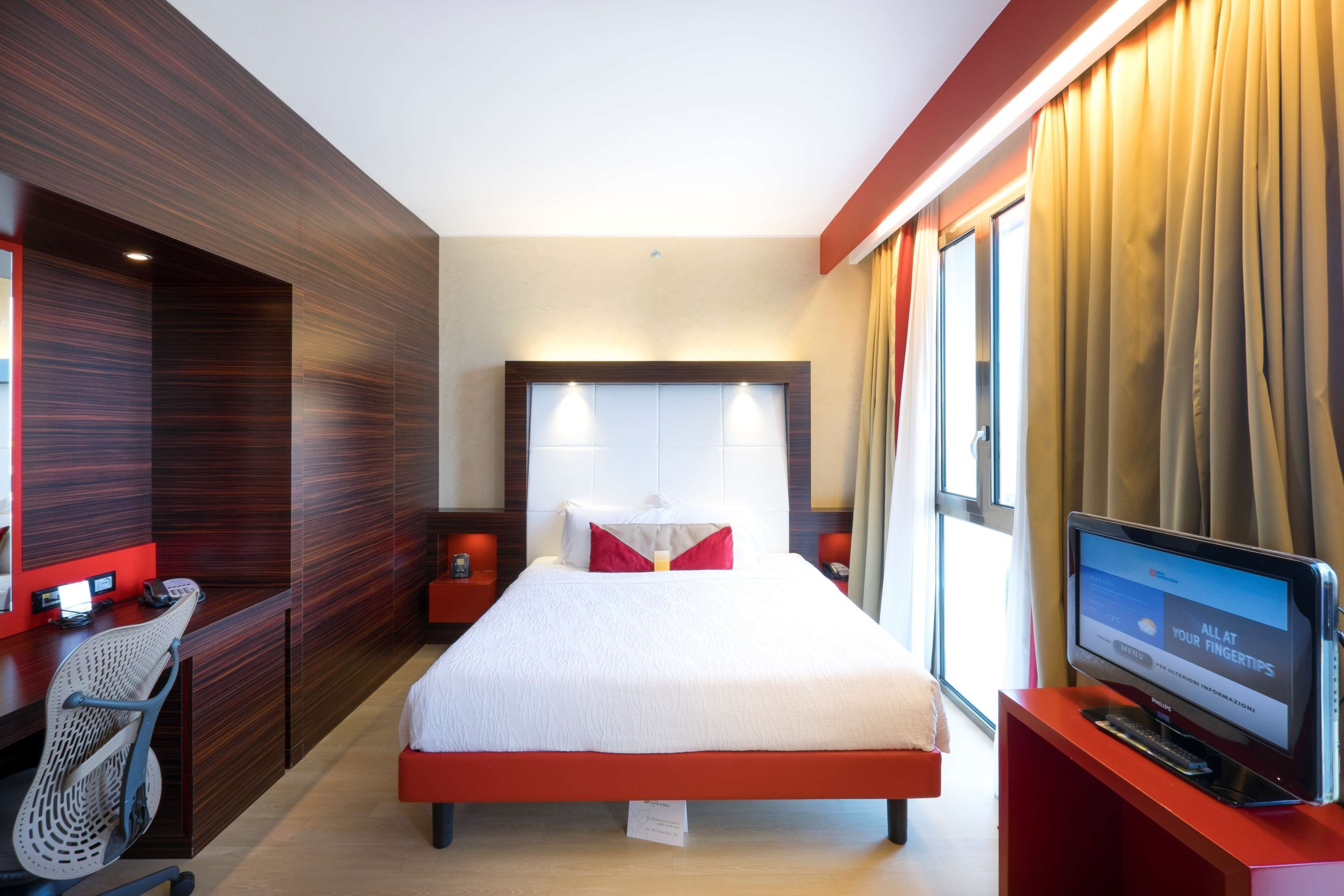 Una camera d'albergo con un letto grande, una scrivania con computer, una sedia e una televisione.