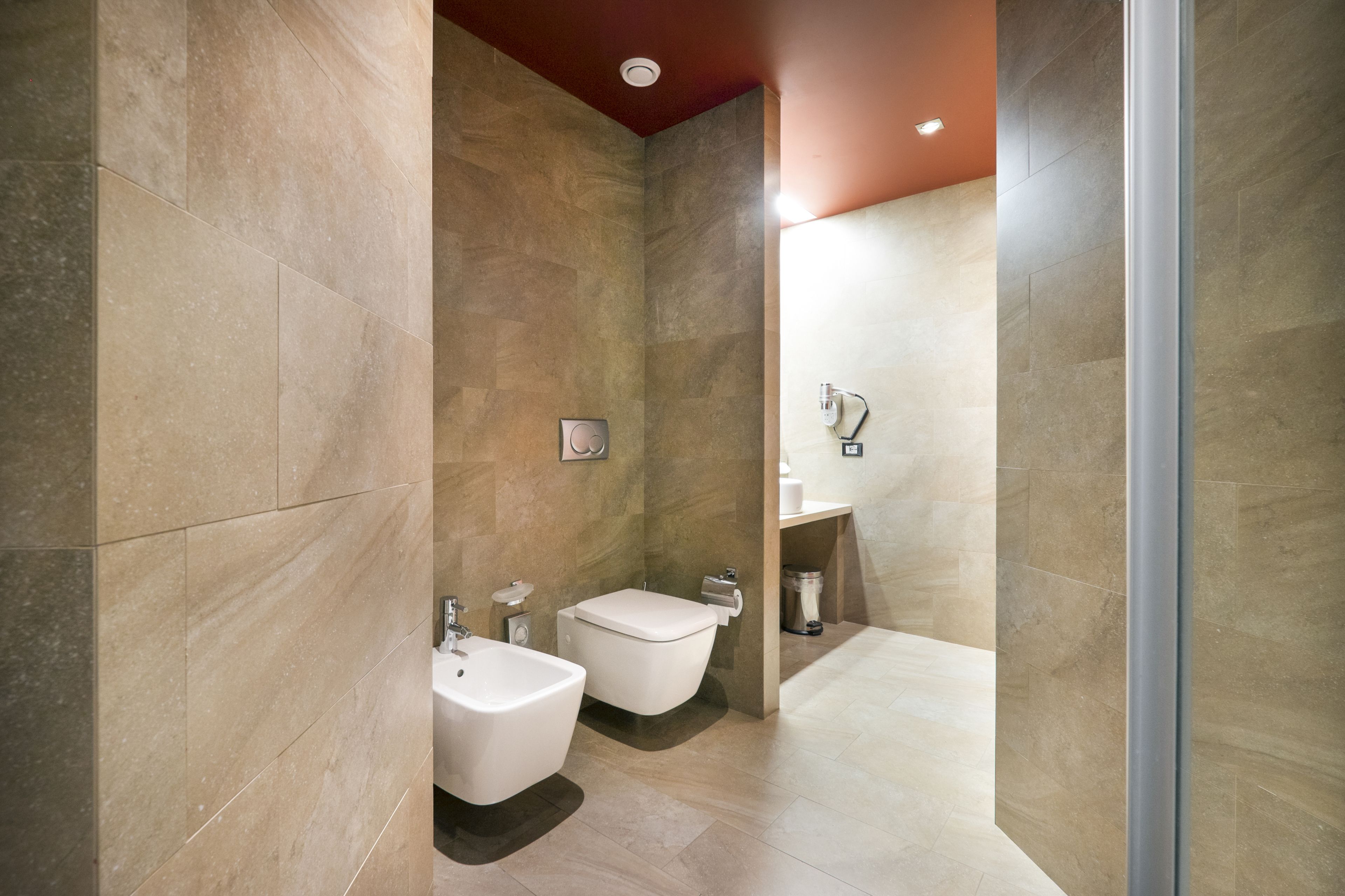 Ein modernes Badezimmer mit einer Bidet-Funktion, Toilette und Waschbecken, mit großen Fliesen und einer Duschkabine aus Glas.