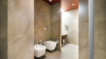 A modern bathroom with a bidet, toilet, and sink, featuring large tiles and a glass shower enclosure.