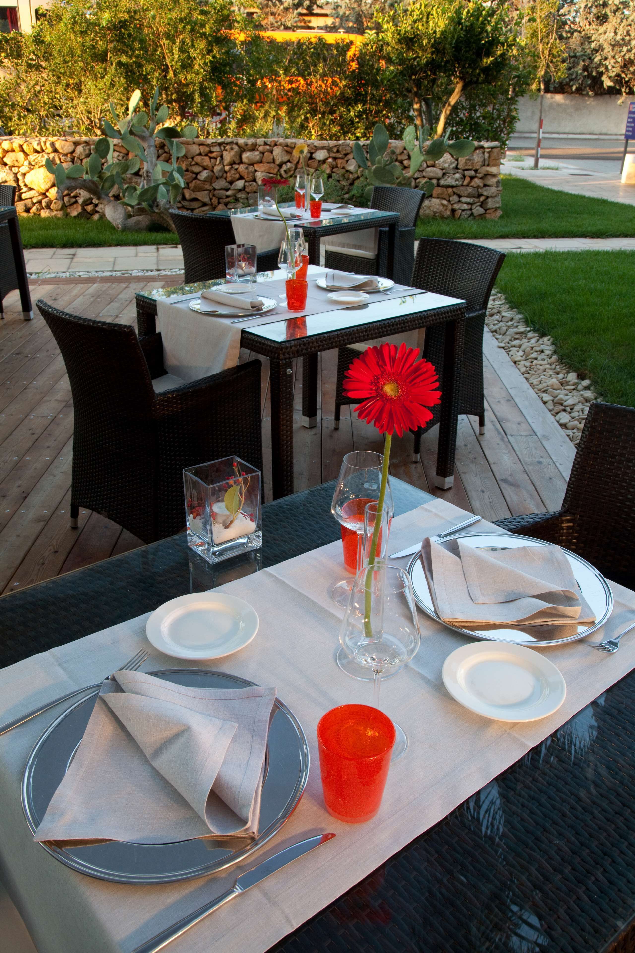 An outdoor dining area with tables set for two, featuring clear glassware, plates, and napkins.