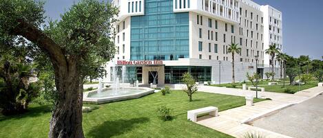 A modern hotel with a central courtyard, a fountain, and a large tree.