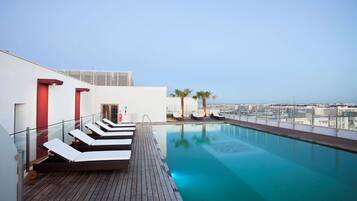 A rooftop pool area with lounge chairs and a clear view of the cityscape.