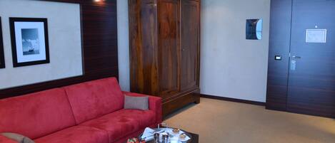 Een hotellobby met een rode bank, een houten kast en een bijzettafeltje met ontbijtartikelen.