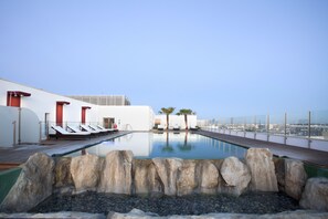 A rooftop pool with lounge chairs, a rock feature, and a city view.