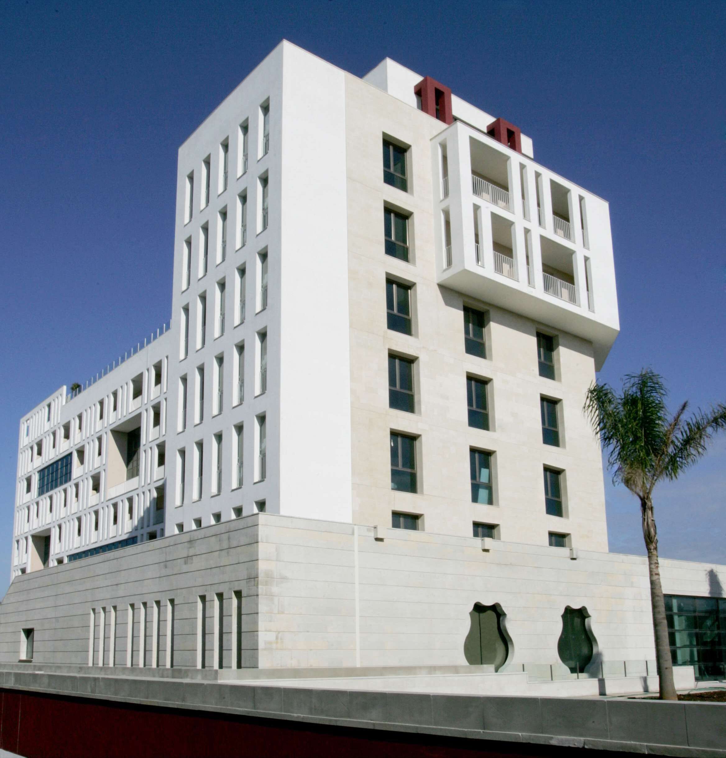 A modern building with a grid-like facade, multiple balconies, and a flat roof.
