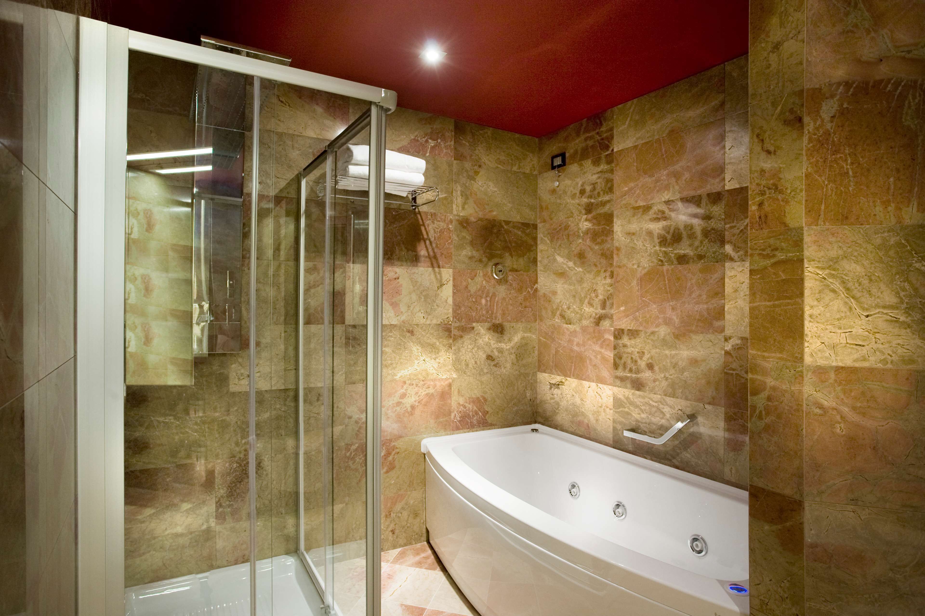 A modern bathroom with a glass-enclosed shower, a freestanding bathtub, and marble walls.
