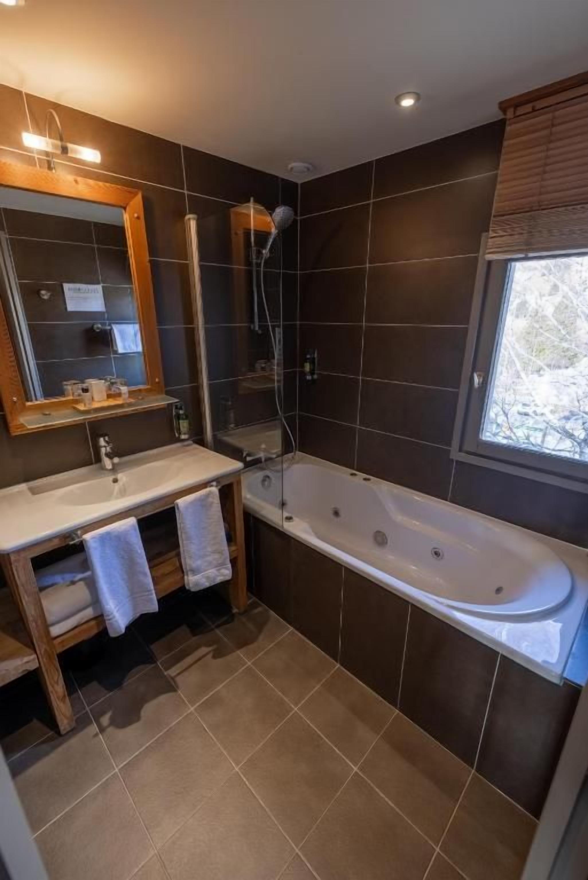 A modern bathroom with a bathtub, a vanity with a mirror, and a window.