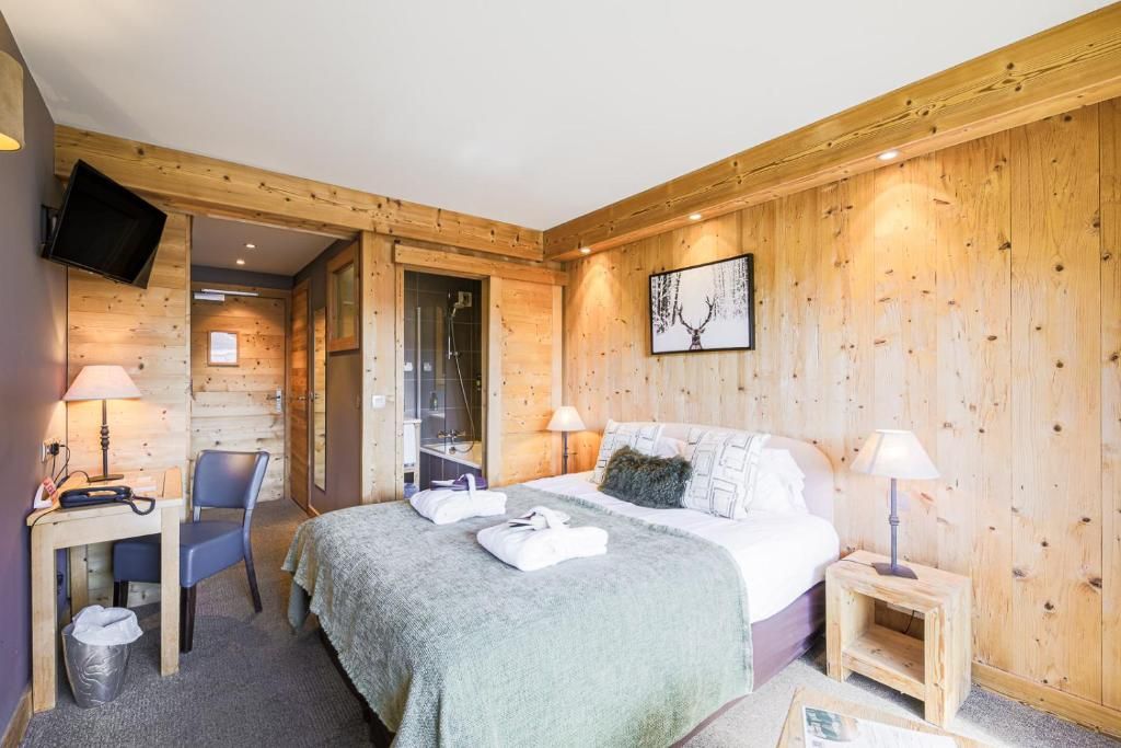 Habitación con paneles de madera, una cama, un escritorio con una silla, un televisor y un baño visible a través de una puerta abierta.