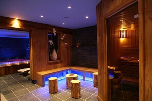 Ein Holzkamin mit Steinwand, Holzbanken und einem kleinen Poolbereich mit Holzstühlen.