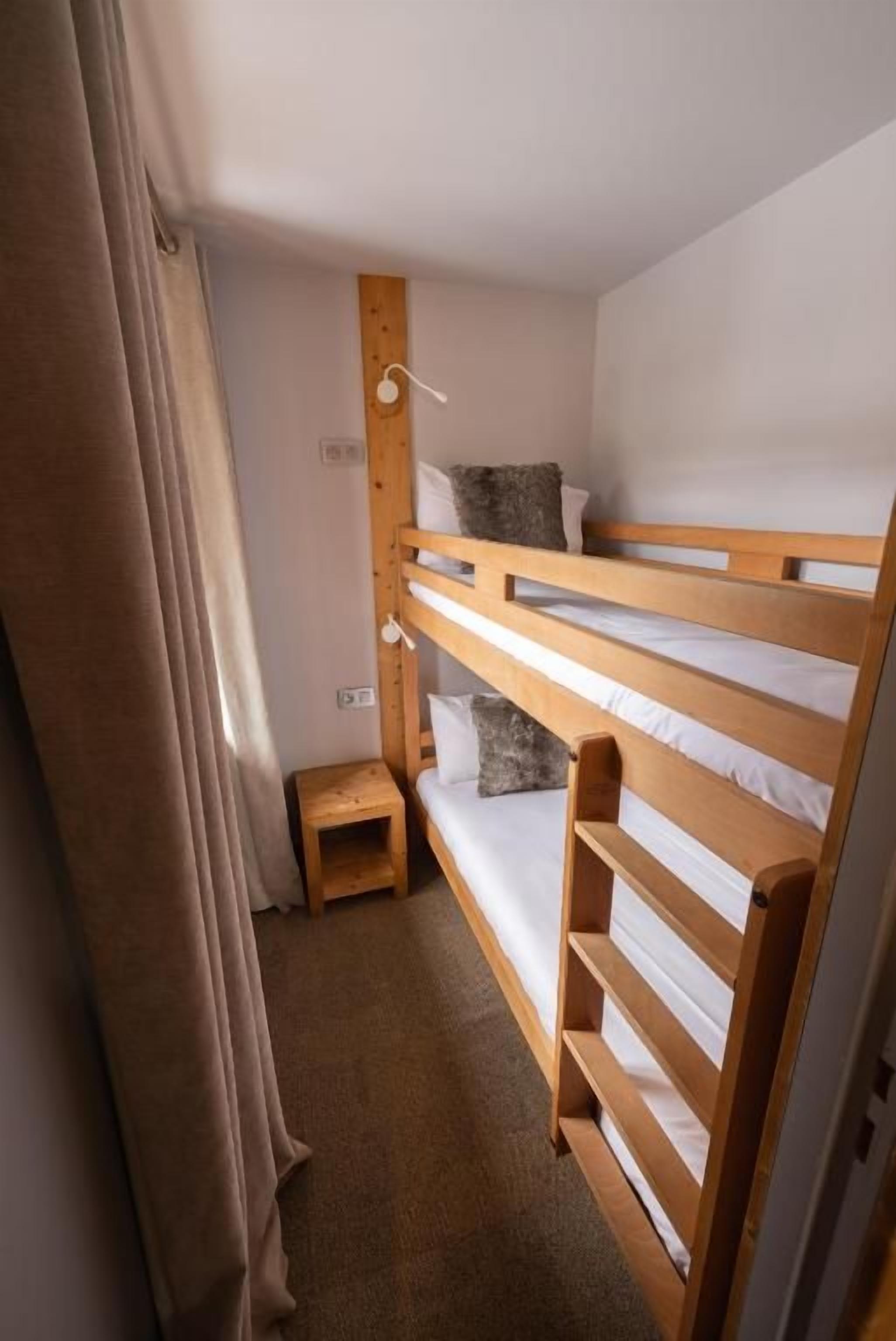 A bunk bed room with a wooden headboard, a small wooden stool, and a single bed with a pillow.