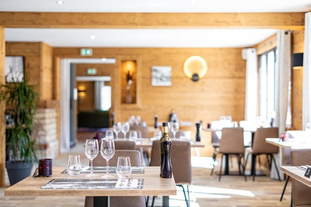 L’intérieur d’un restaurant avec des murs en bois, des tables dressées avec des verres à vin et une bouteille de vin posée sur la table.