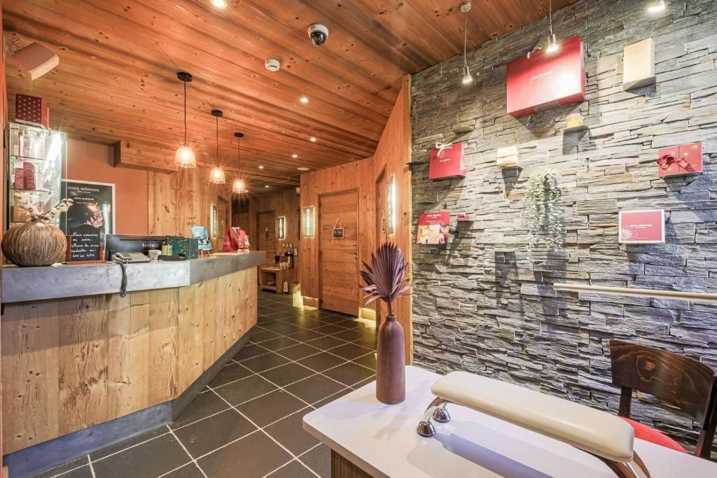 A reception area with a wooden counter, stone wall decorations, and a vase with a decorative plant.