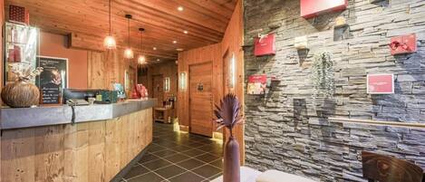 Zona de recepción con mostrador de madera, adornos en la pared de piedra y un jarrón con planta decorativa.