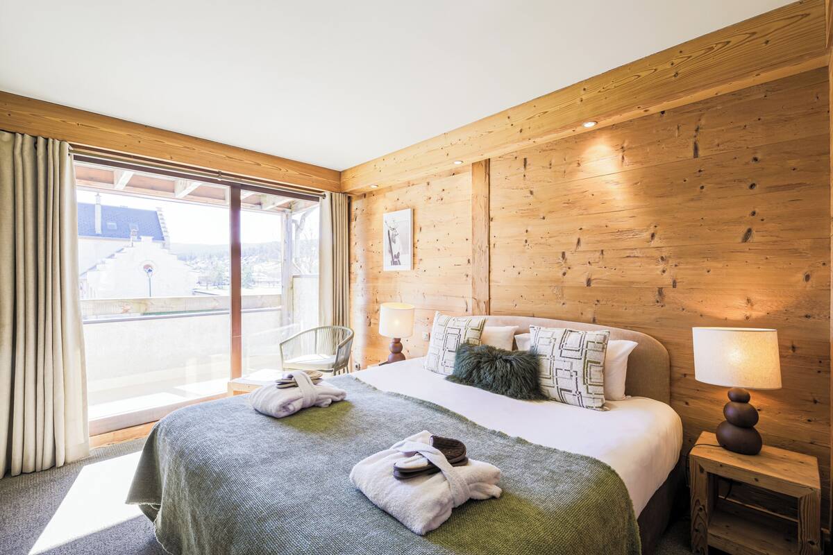 Une chambre d’hôtel avec un grand lit, des murs en bois, une fenêtre avec des rideaux et une vue sur un bâtiment à l’extérieur.